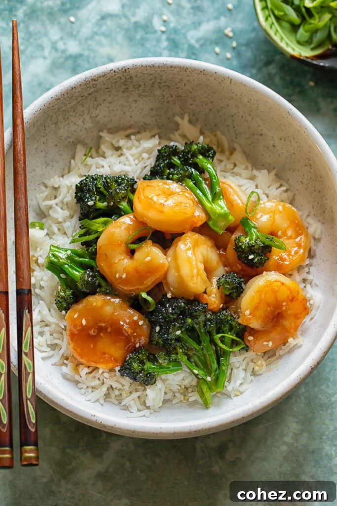 Top down shot of shrimp and broccoli stir fry with rice in a bowl, accompanied by chopsticks, ready to eat.