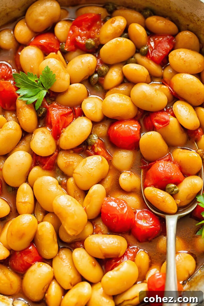 Close up shot of butter beans and tomato sauce topped with fresh basil with a spoon
