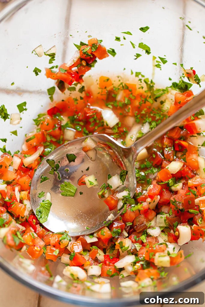 Top down shot of pico de gallo in a glass bowl with a serving spoon, highlighting the chunky texture and fresh ingredients.
