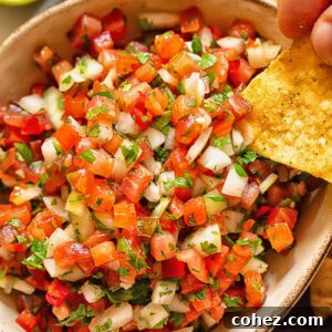 Close up shot of tortilla chip dipped in pico de gallo, showcasing the fresh, chunky texture of the salsa.