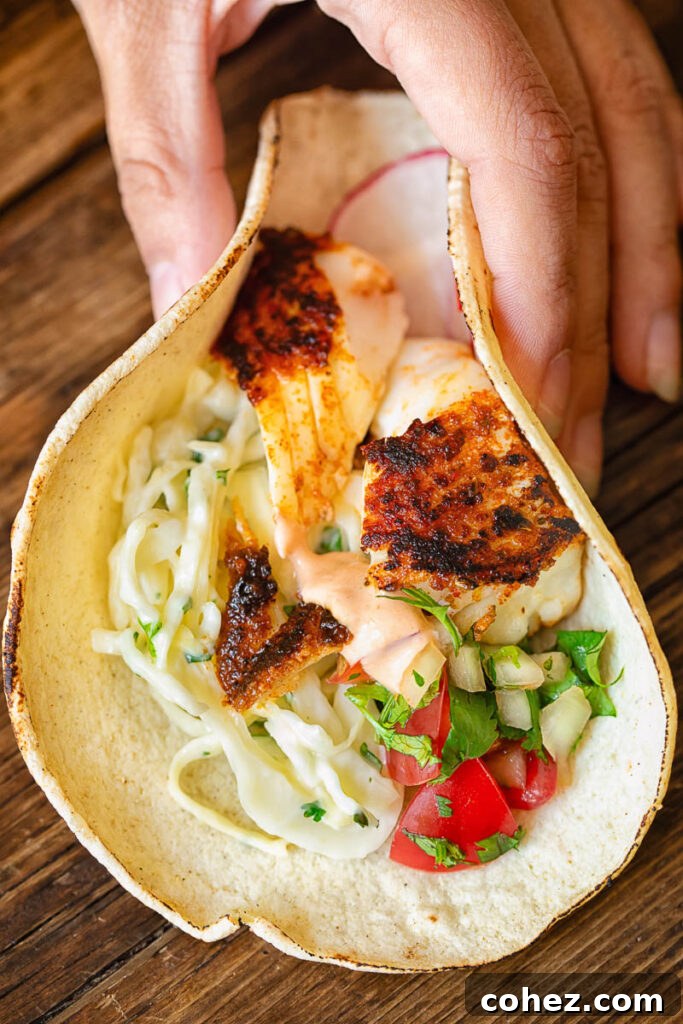 Cajun Fish Tacos 5 A hand gently folding a corn taco filled with blackened fish and fresh toppings