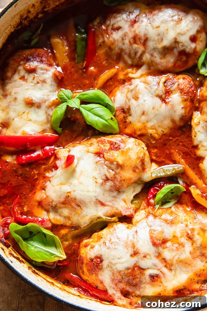 Close-up of baked chicken marinara garnished with fresh basil, showing the rich red sauce, colorful bell peppers, and succulent chicken beneath a blanket of melted cheese.