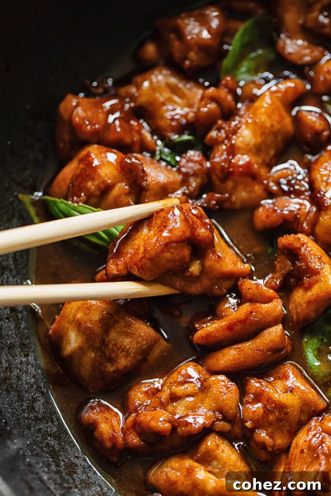 Chopsticks lifting a piece of tender, glazed Three Cup Chicken from a serving bowl, showcasing its sticky texture.