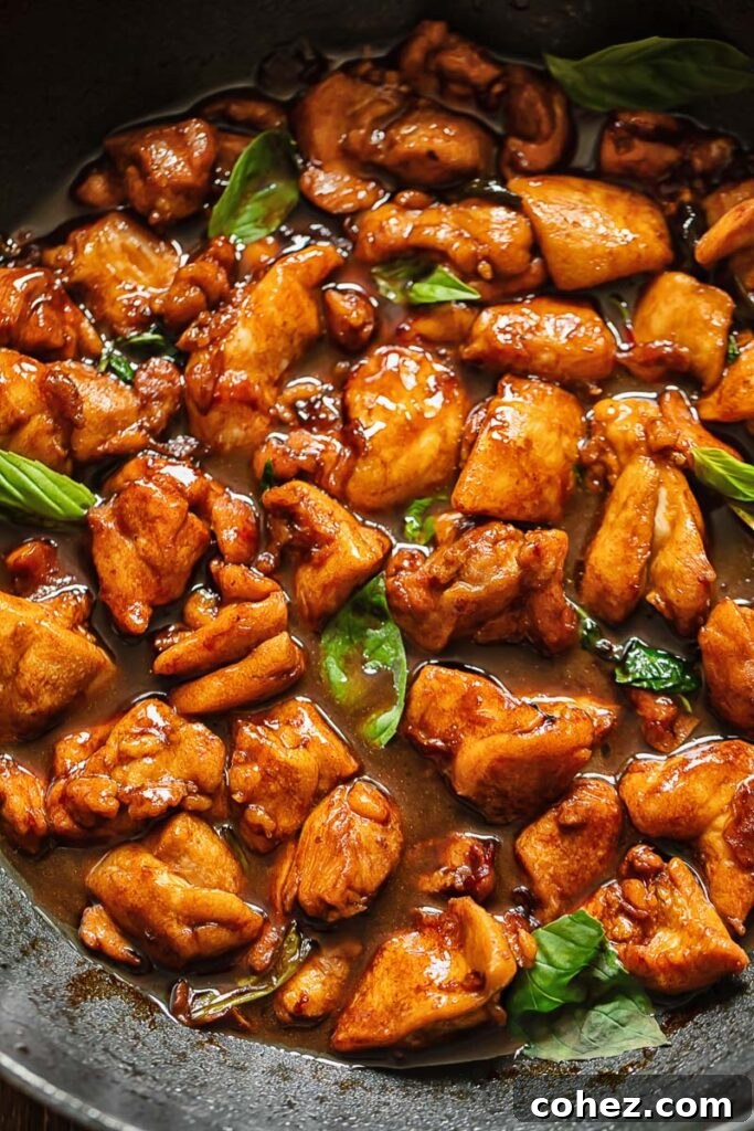 A close-up shot of the vibrant Three Cup Chicken stir-fry, showcasing the tender chicken pieces, aromatic basil, and rich, dark sauce in a pan.