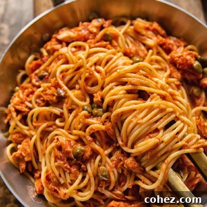 Top-down view of spaghetti in red sauce with tuna and capers in a pan