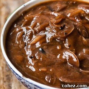 Side view of a serving bowl filled with rich, dark red onion gravy, ready to be poured over a holiday meal.