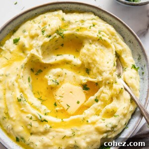 Herby mashed potatoes with a dollop of melted butter in the center, garnished with fresh herbs, in a rustic bowl.