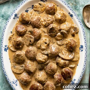 Hearty meatballs coated in a luxurious, creamy mushroom stroganoff sauce, served on an elegant white and blue platter.