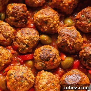 Succulent pork and beef meatballs simmering in a vibrant tomato sauce, garnished with olives and red pepper slices, in a rustic pot.