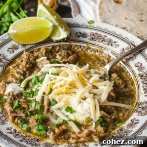 Chili Verde in a bowl topped with grated cheese and chopped cilantro, showcasing its vibrant green hue.