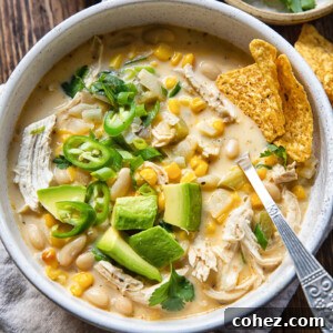 Top down view of creamy white chicken chili, garnished with corn, chilies, and avocado in a bowl.