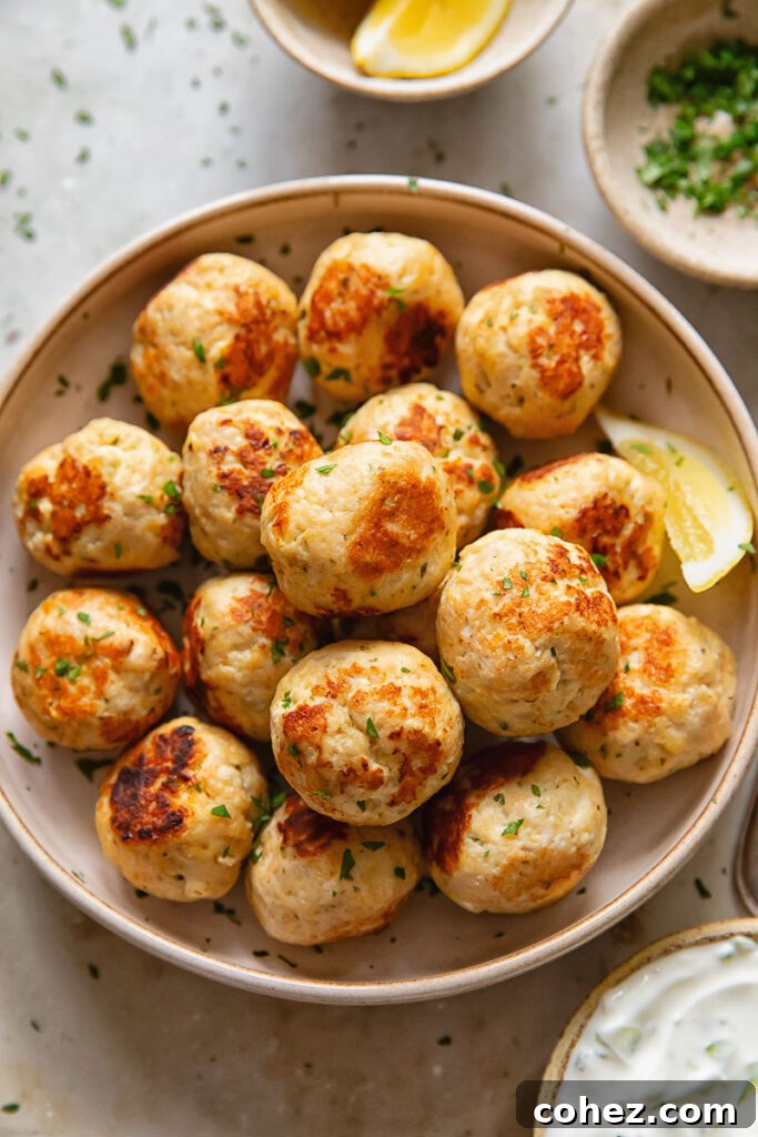 Top down view of a large bowl filled with golden-brown chicken feta meatballs, garnished with fresh herbs and a side of creamy tzatziki dip.