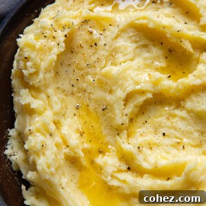 Top-down shot of creamy mashed potatoes swirled artfully on a small plate, generously topped with grated Parmesan cheese and freshly ground black pepper.