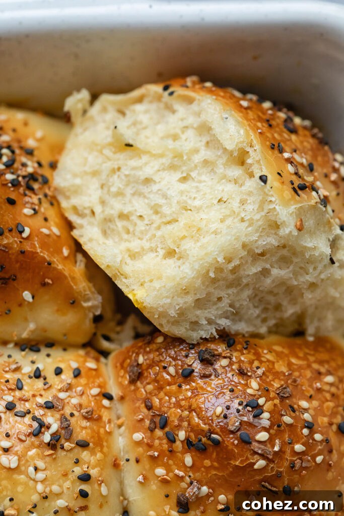 Wake Up To Everything Bagel Dinner Rolls 3 Close-up shot of a hand gently removing a golden, fluffy dinner roll from a baking dish, highlighting the soft interior and crispy Everything Bagel crust.