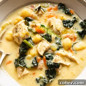 Creamy chicken gnocchi soup in a light-colored bowl with a spoon, showing spinach, chicken, and gnocchi.