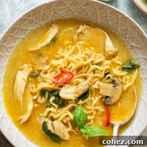 Thai chicken noodle soup in a bowl with chopsticks, featuring coconut broth, noodles, chicken, and greens.
