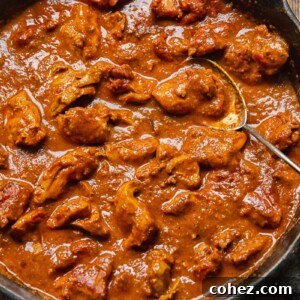 Close up of a pan of rich, vibrant Chicken Rogan Josh with a serving spoon, inviting to be enjoyed.