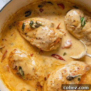 A top-down view of tender chicken breast simmering in a rich, creamy tomato sauce in a rustic pan, garnished with fresh herbs.