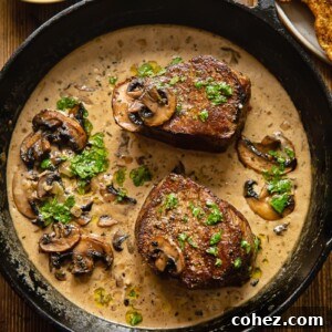 A top-down view of two perfectly cooked filet mignon steaks resting in a rich, savory mushroom marsala sauce in a rustic cast iron pan.