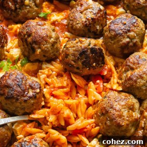 Close-up shot of a one-pan Greek baked orzo with juicy meatballs, bubbling in a rich tomato sauce, topped with feta.