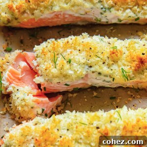 Close up shot of three salmon fillets on a baking sheet, generously topped with a creamy herb and garlic mixture and golden Panko breadcrumbs.
