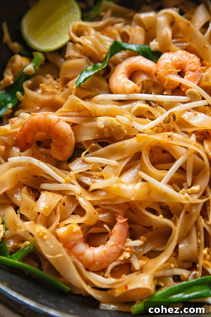 Close-up of Shrimp Pad Thai noodles adorned with shrimp, bean sprouts, green onions, and a fresh lime slice.