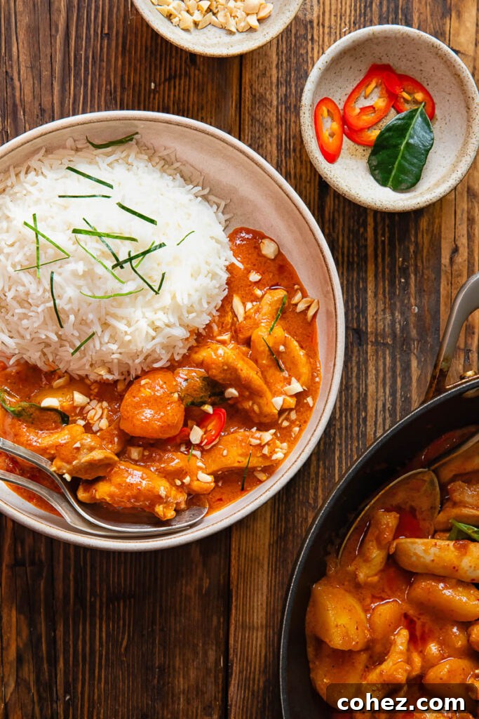 A generous serving of Panang Chicken Curry with steamed jasmine rice in a bowl, set against a rustic wooden background.