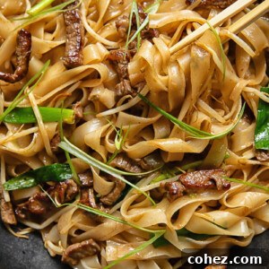 Top down shot of chop sticks picking up chow fun noodles with beef and beansprouts from a pan