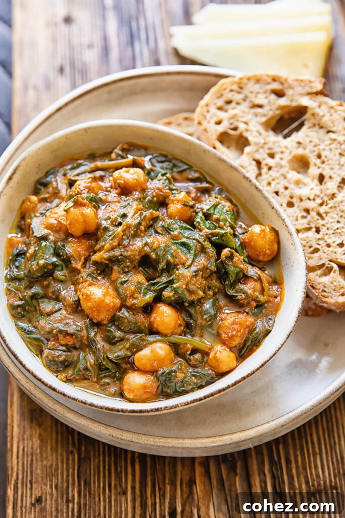 A bowl of Spanish spinach and chickpea stew served with slices of crusty bread on a plate.