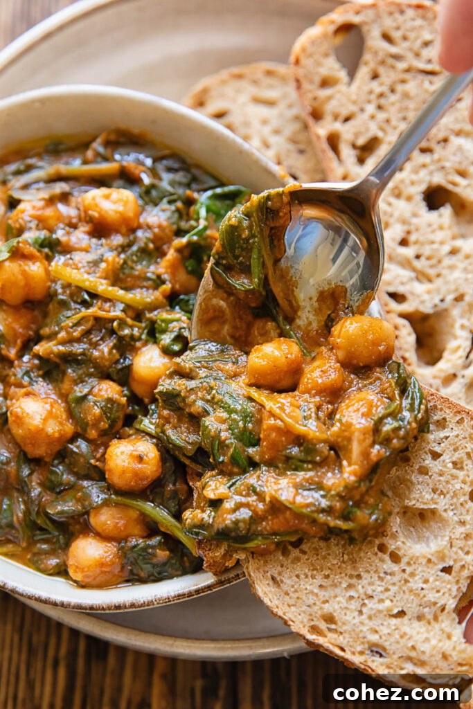 A spoonful of Spanish spinach and chickpea stew being scooped from a bowl onto a piece of bread.
