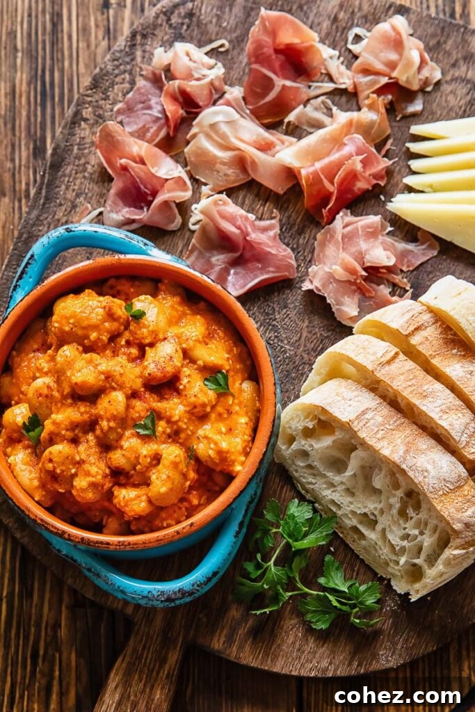An overhead shot of a tapas table featuring butter beans in Romesco sauce, sliced bread, and cheese.