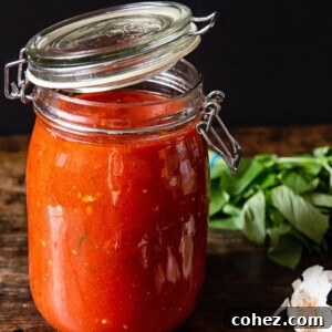 Jar of red sauce next on a wooden table with garlic and basil