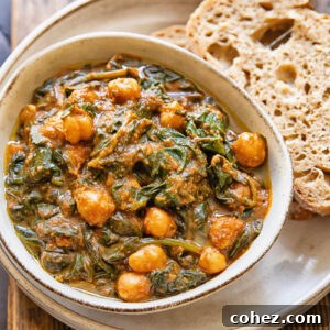 Top down view of a bowl of chickpeas and spinach, on top of a serving plate with a couple slices of bread.