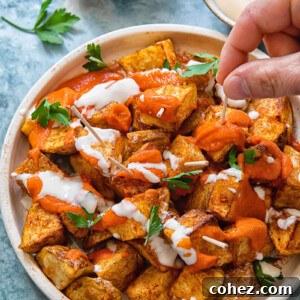 Top down view of fried potato chunks with two sauce drizzled over with a hand picking up a piece