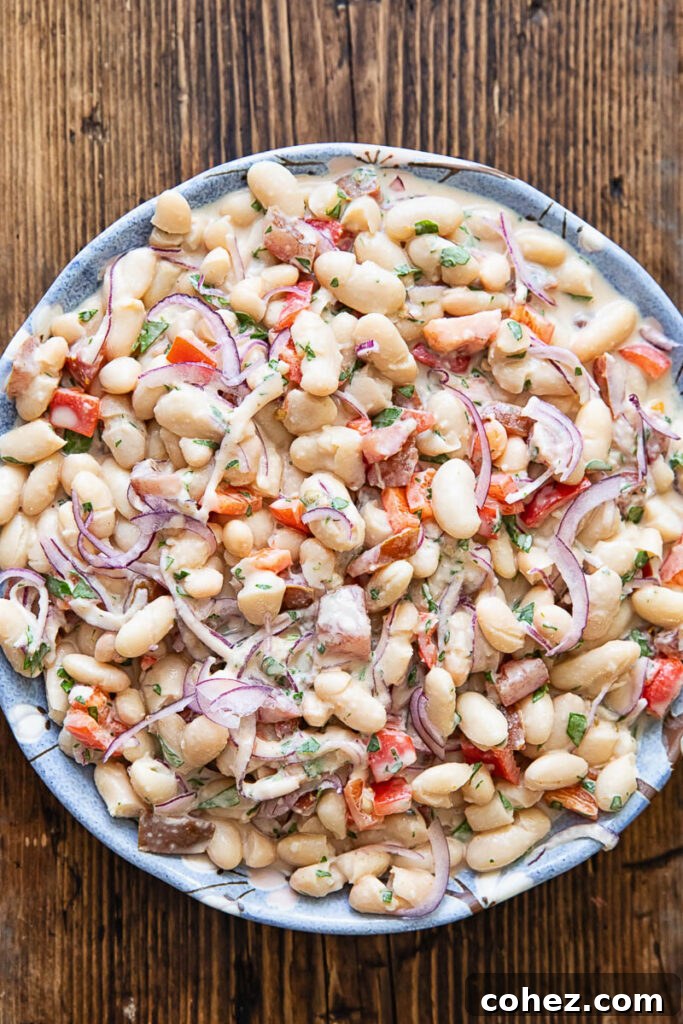Top down photo of the bean salad in a white bowl on a dark wood background.
