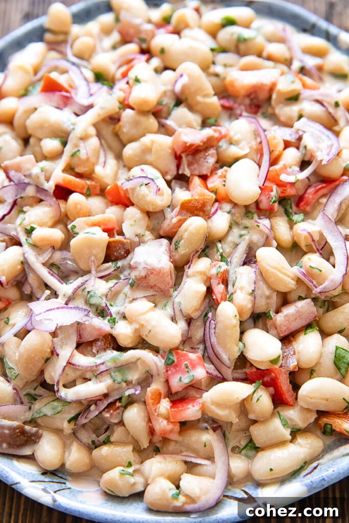 close up photo of the salad showing beans, onions and peppers with herbs and a creamy dressing.