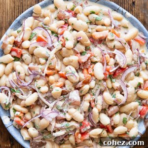 Top down photo of the bean salad in a white bowl on a dark wood background.