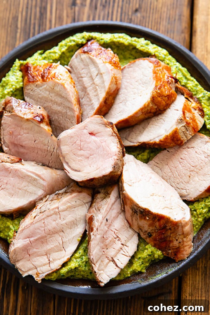 Slices of pork tenderloin on a bed of green sauce, on a plate with a dark wood background.