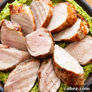 Slices of pork tenderloin on a bed of green sauce, on a plate with a dark wood background.