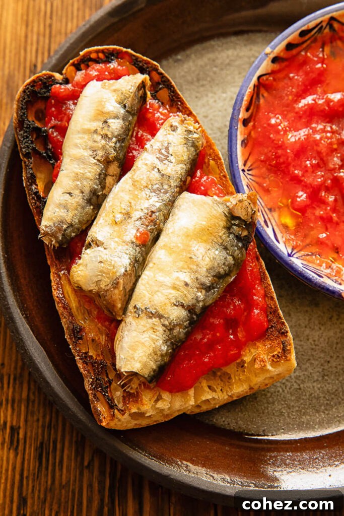 A dark plate with toast, sardines and tomato mixture.