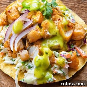 Close up of a tostada with white fish covered in salsa, coleslaw, onion slices and cilantro, on a wooden background.