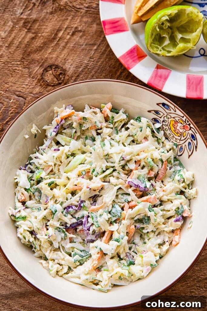 Close up of slaw in a bowl on a wooden background, next to a colourful plate with a lime half.