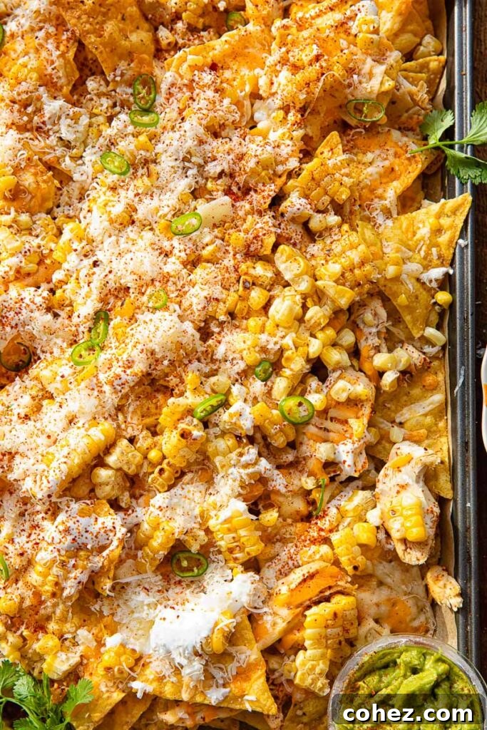 Close up of a baking sheet with nachos, with corn, jalapeños, corn and Tajin seasoning.